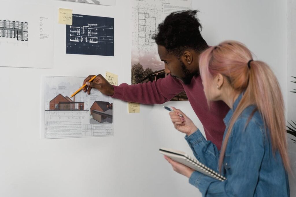 two people pointing at building blueprints on white wall