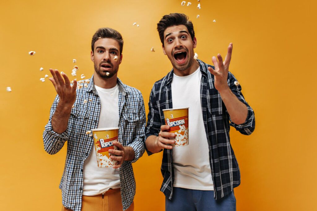 Image depicting 2 men scattering popcorn getting ready to watch a movie on an ott service 