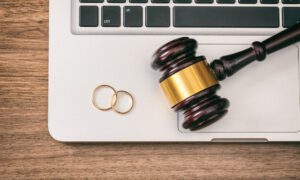 Divorce concept. Wedding rings and judge gavel on computer laptop, wooden background, top view