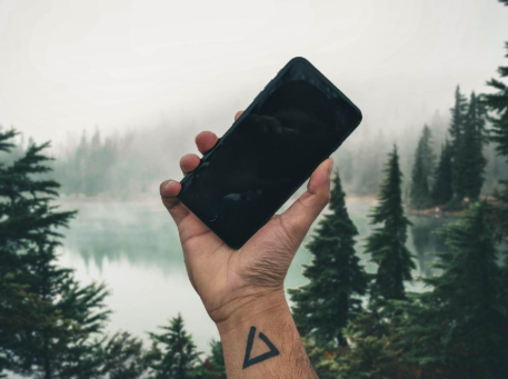 Tattooed hand holding a smartphone among the trees of a misty forest