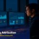 Marketing attribution technology professional analyzing multi-touch ROI dashboards on dual monitors in modern office