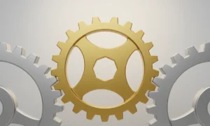 Golden uniquely shaped gear meshing between two silver gears on a soft neutral background.