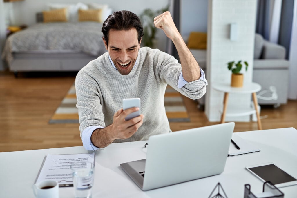 Person celebrating while checking a smartphone after improving their credit score with rent payment reporting and credit monitoring tools.