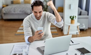 Person celebrating while checking a smartphone after improving their credit score with rent payment reporting and credit monitoring tools.