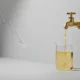 Brass valve pours a golden stream into a glass beaker; faint downward trend line in soft gray background.