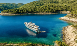 Luxury crewed yacht anchored in Croatia's Kornati National Park with crystal-clear turquoise water, rocky islands and guests enjoying dinner on deck at sunset.