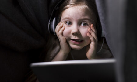 A girl uses a tablet while parents protect her from child identity theft and online identity risks.